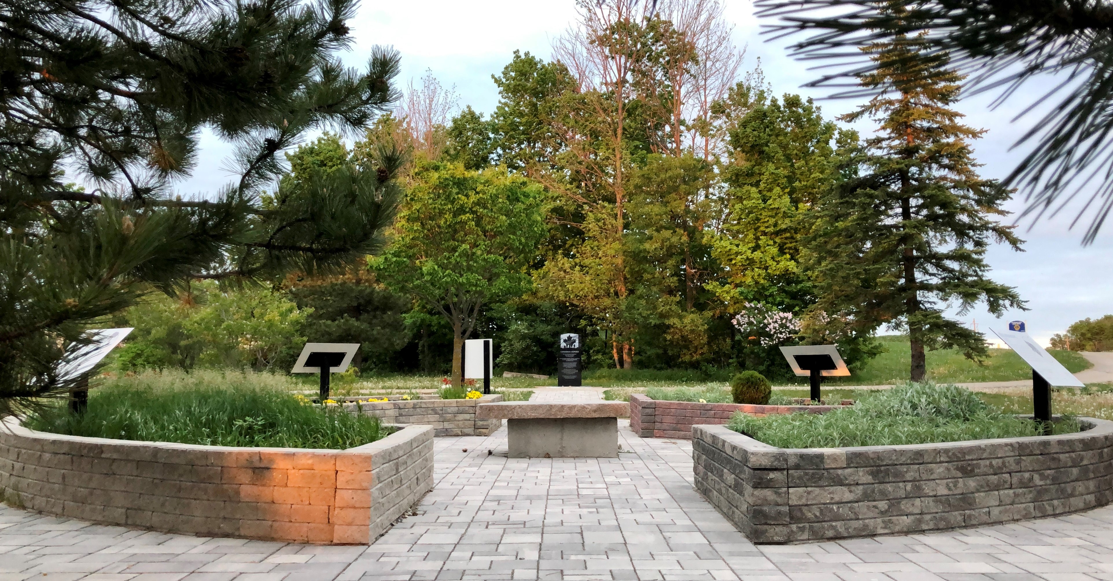 Garden with four raised beds arranged in a circle surrounded by trees. A stone table sits in the middle of the circle.